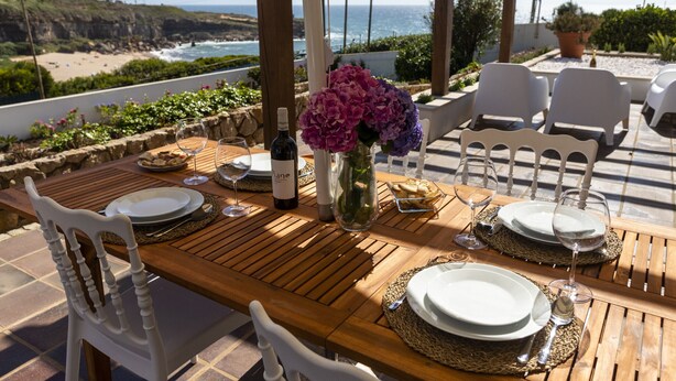 A wooden table set for dining with white chairs, a vase with flowers, and a bottle of wine. - Villa S. Lourenço by ACasaDasCasas (Ericeira)