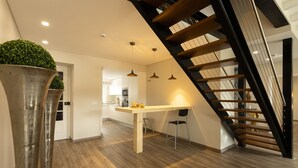 A modern kitchen with wooden flooring, a dining table, and a staircase with black railings. - Villa S. Lourenço by ACasaDasCasas (Ericeira)