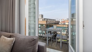En balkon med et bord og stole, udsigt til bygninger, og et vindue med gardiner.