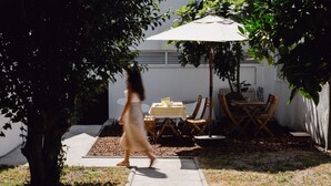 A patio area with a table and chairs under a large umbrella, surrounded by trees.