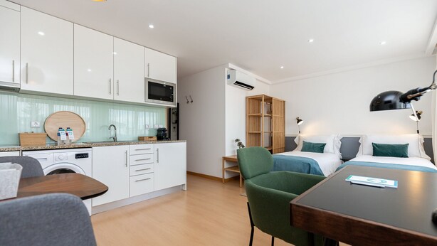 A compact hotel room with a kitchenette, a dining area, and a bed with a nightstand.