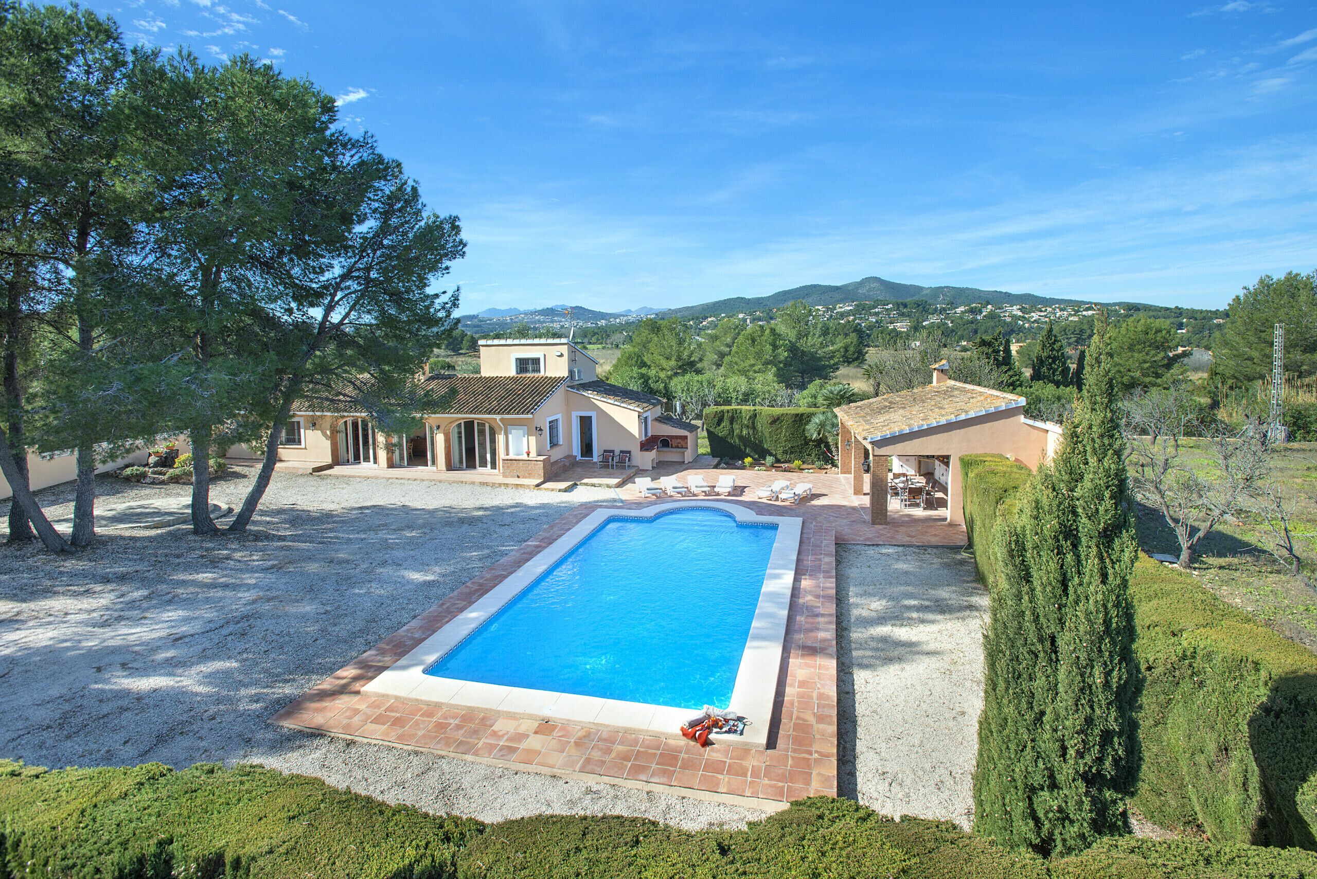 A swimming pool surrounded by a gravel area, with a house and trees in the background.