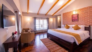 A hotel room with a large bed, a desk, a chair, a TV, and a brick wall. - Hotel Bhadgaon (Bhaktapur)