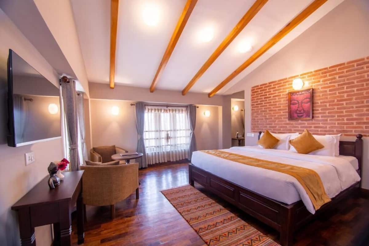 A hotel room with a large bed, a desk, a chair, a TV, and a brick wall.