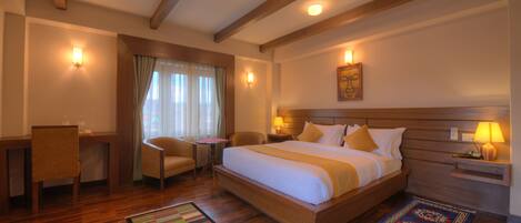 Une chambre d’hôtel avec un grand lit, une tête de lit en bois, des lampes de chevet, un bureau, une chaise et une fenêtre avec des rideaux.