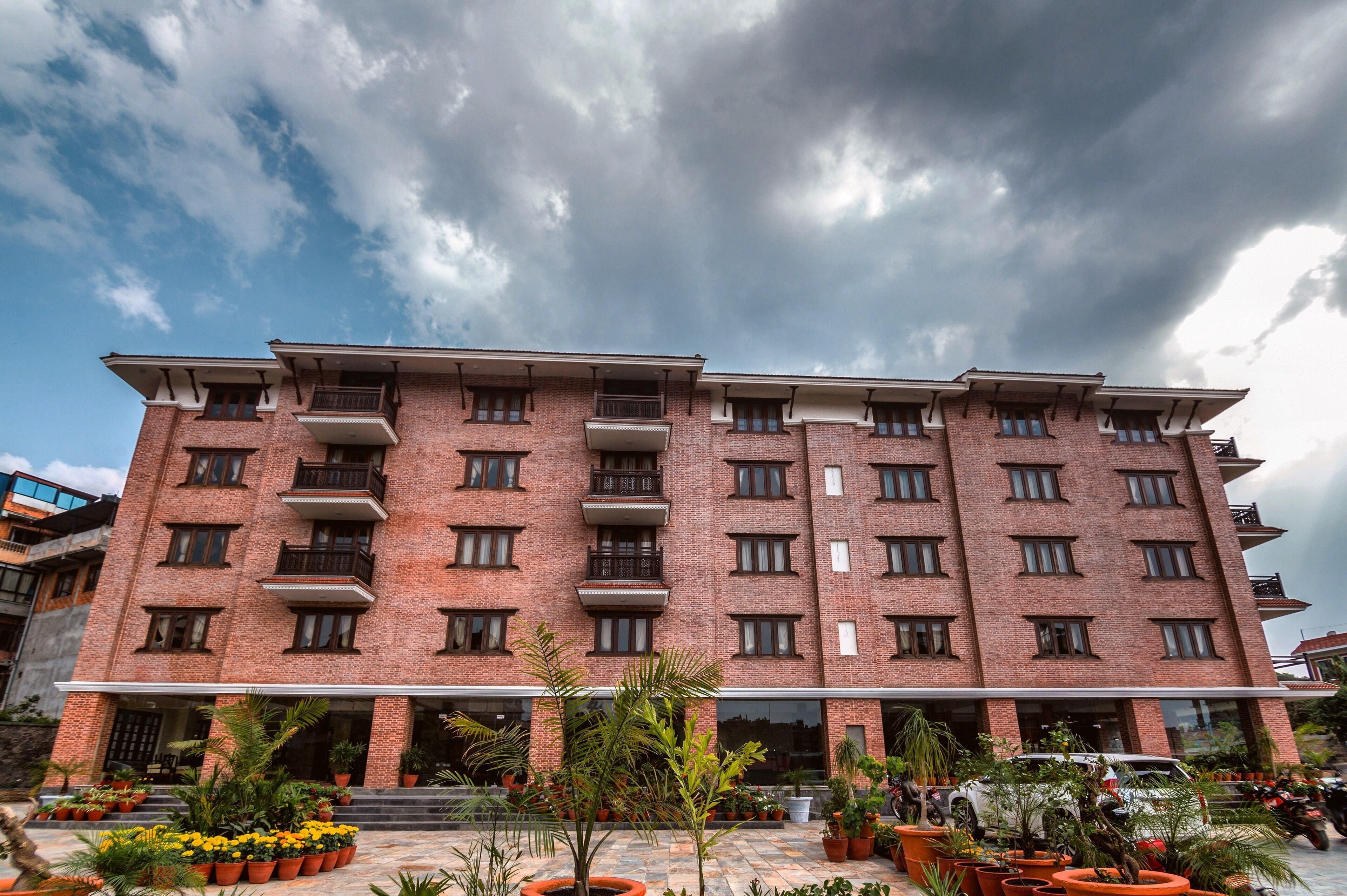 A multi-story brick building with balconies, a covered entrance, and potted plants in the foreground.