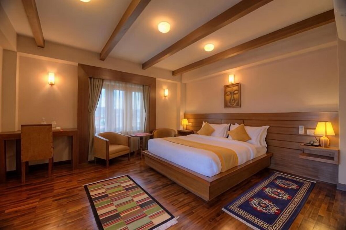 A hotel room with a large bed, a desk, a chair, and a nightstand with a lamp.
