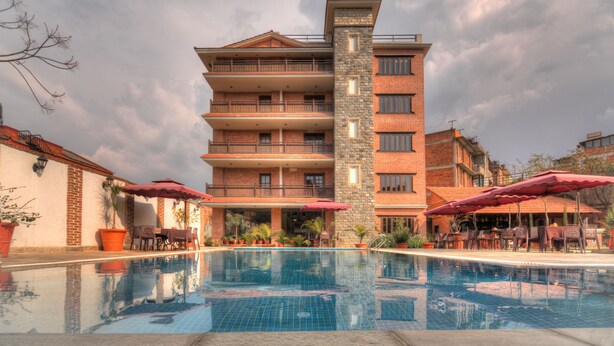 A hotel with a swimming pool, outdoor seating, and a multi-story building with balconies. - Hotel Bhadgaon (Bhaktapur)