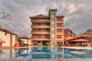 Un hotel con piscina, mobiliario exterior y un edificio de varios pisos con balcones.