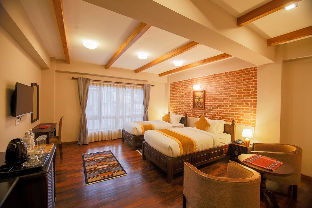 A hotel room with two beds, a desk with a coffee maker, a TV, and a brick wall.