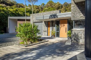 Una casa moderna con fachada de piedra, puerta de madera y un pequeño jardín con un árbol y una planta en maceta.