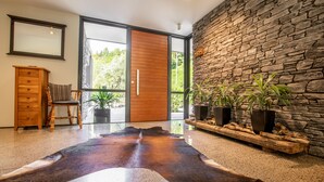 Un intérieur moderne avec un mur en pierre, une porte en bois, un tapis en cuir, une chaise en bois et des plantes en pot.