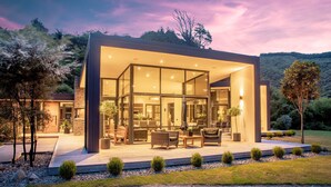 Une maison moderne dotée d’une façade en verre, d’un espace extérieur aménagé pour se détendre et d’un jardin paysager.