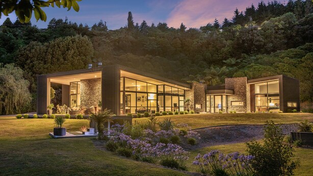 Une maison moderne dotée de grandes baies vitrées, d’une façade en pierre et d’un jardin bien entretenu.