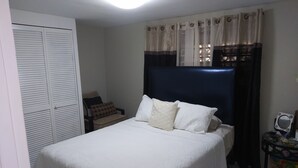 Een net opgemaakt bed met witte lakens, een donker hoofdbord en een raam met gordijnen.