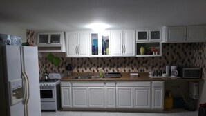 Een keuken met witte kastjes, een fornuis, een spoelbak en een magnetron.