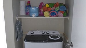 Een wasserij met een wasmachine, gestapelde handdoeken en schoonmaakmiddelen.