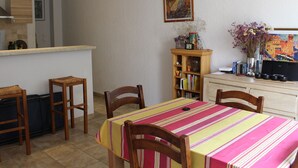 Un coin repas avec une table recouverte d’une nappe à rayures, des chaises en bois, une bibliothèque et un tableau accroché au mur.