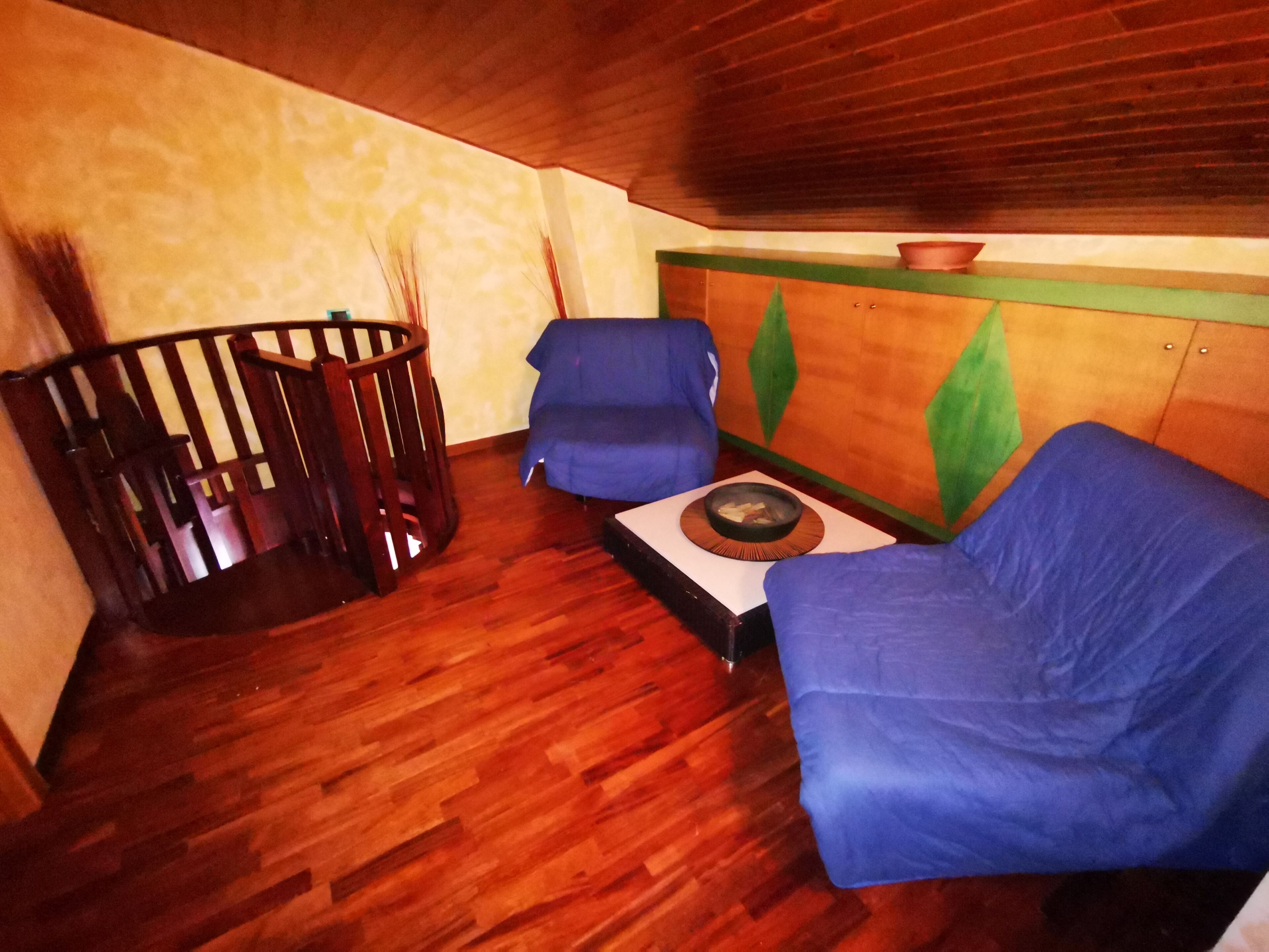 A room with a wooden floor, a blue sofa, a wooden chair, and a small table with a bowl.