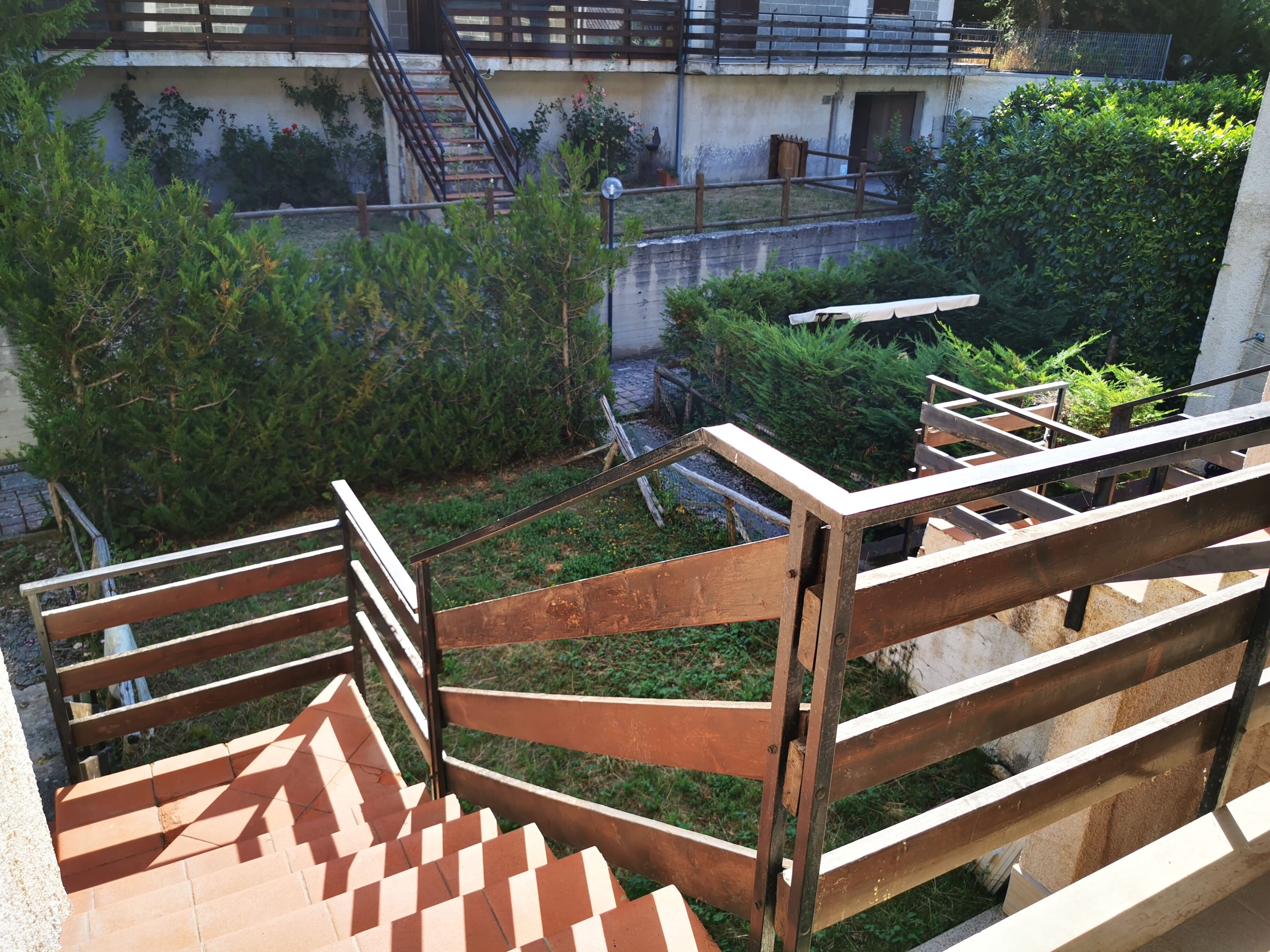 Eine Treppe mit Holzgeländern führt zu einem Dachgarten mit Grünpflanzen und Blick auf ein Gebäude im Hintergrund.