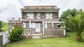Una casa de dos pisos con un balcón, un porche pequeño y un jardín.