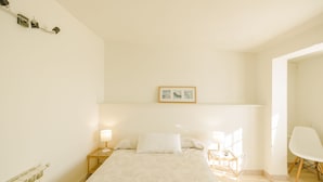 Un dormitorio con cama, lámparas de noche, una silla e imagen enmarcada en la pared.