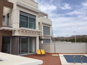 A modern building with a rooftop pool, two yellow lounge chairs, and a clear view of the surrounding landscape.