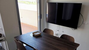 Ett modernt matområde med ett träbord, fyra stolar, en platt-TV som är monterad på väggen och en dörr som leder ut till ett utomhusområde.
