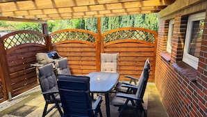 Une terrasse couverte avec une table et des chaises, un barbecue et une clôture en bois.