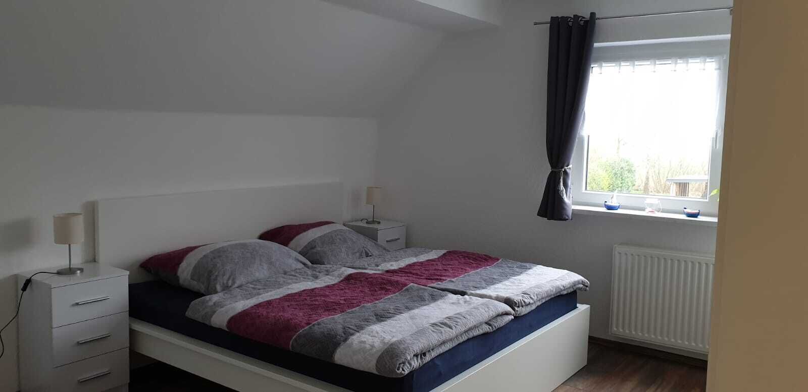 Et soveværelse med seng, sengeborde, et vindue med gardiner og en radiator.