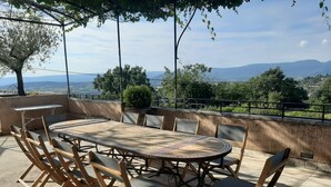 An outdoor patio with a round table and chairs, surrounded by a stone wall and a metal railing, overlooking a scenic landscape. - Restored farmhouse with heated pool and landscaped gardens. (Apt)