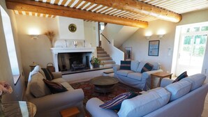 A cozy living room with a fireplace, a staircase, and a comfortable seating area. - Restored farmhouse with heated pool and landscaped gardens. (Apt)
