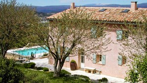 A pink building with a tiled roof, a swimming pool, and a tree in the foreground. - Restored farmhouse with heated pool and landscaped gardens. (Apt)