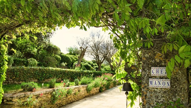A stone pathway leading through a lush garden with neatly trimmed hedges and a sign reading "CHEZ MANON". - Restored farmhouse with heated pool and landscaped gardens. (Apt)