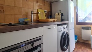A compact kitchen with a washing machine, a small sink, and a window with a view. - Cozy studio in Collioure with sunny terrace (Collioure)