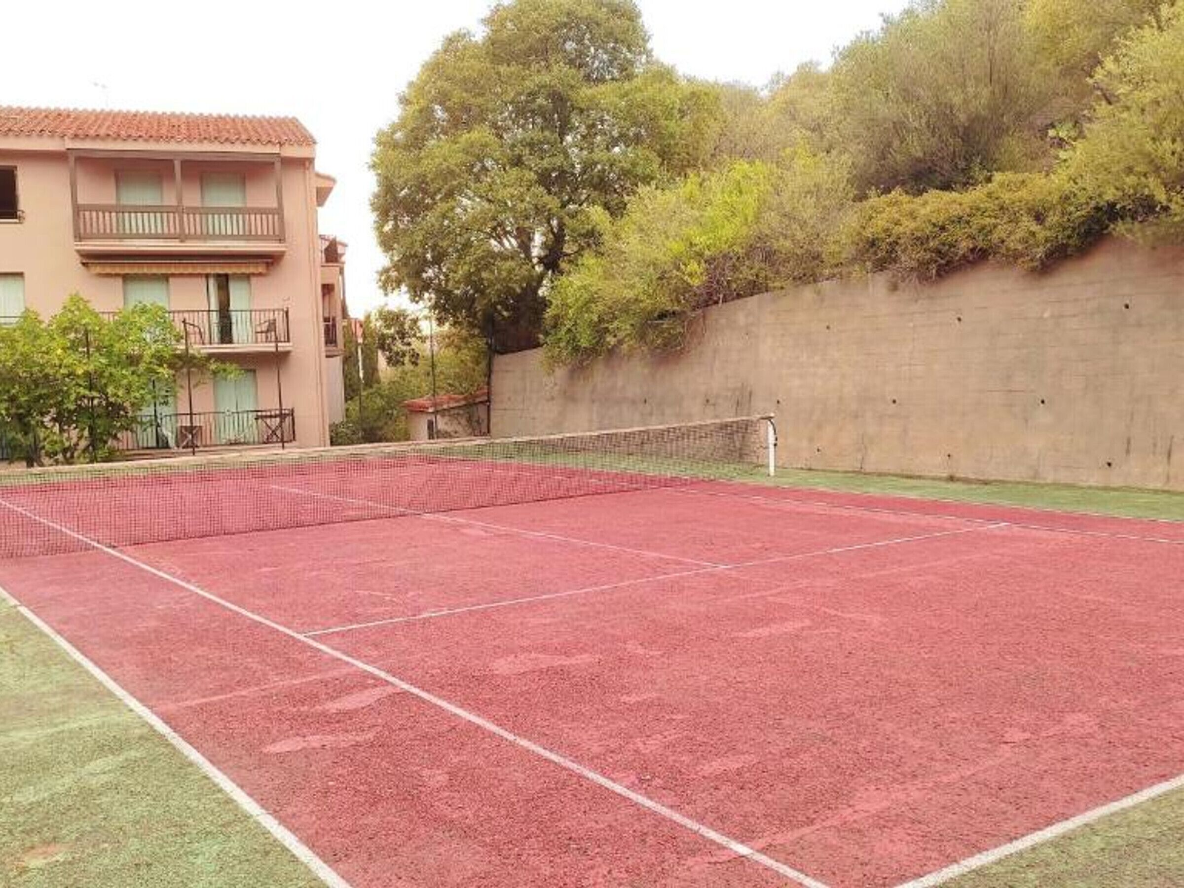 Un court de tennis avec un filet, entouré d’un mur en béton et d’arbres.