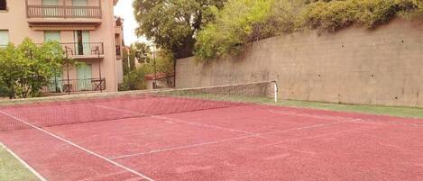 Un court de tennis avec un filet, entouré d’un mur en béton et d’arbres.