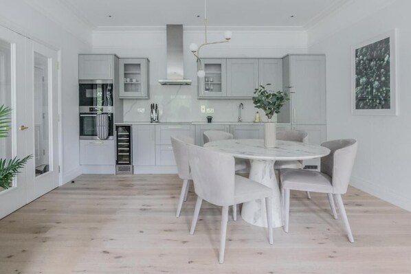 A modern kitchen with white cabinetry, a marble island, and a dining area with a round table and chairs.