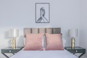 A bedroom with a bed, two bedside tables with lamps, and a framed artwork on the wall.