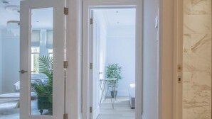 A hallway with a white door leading to a room with a bed and a potted plant. - Bright 3-room apartment (London)