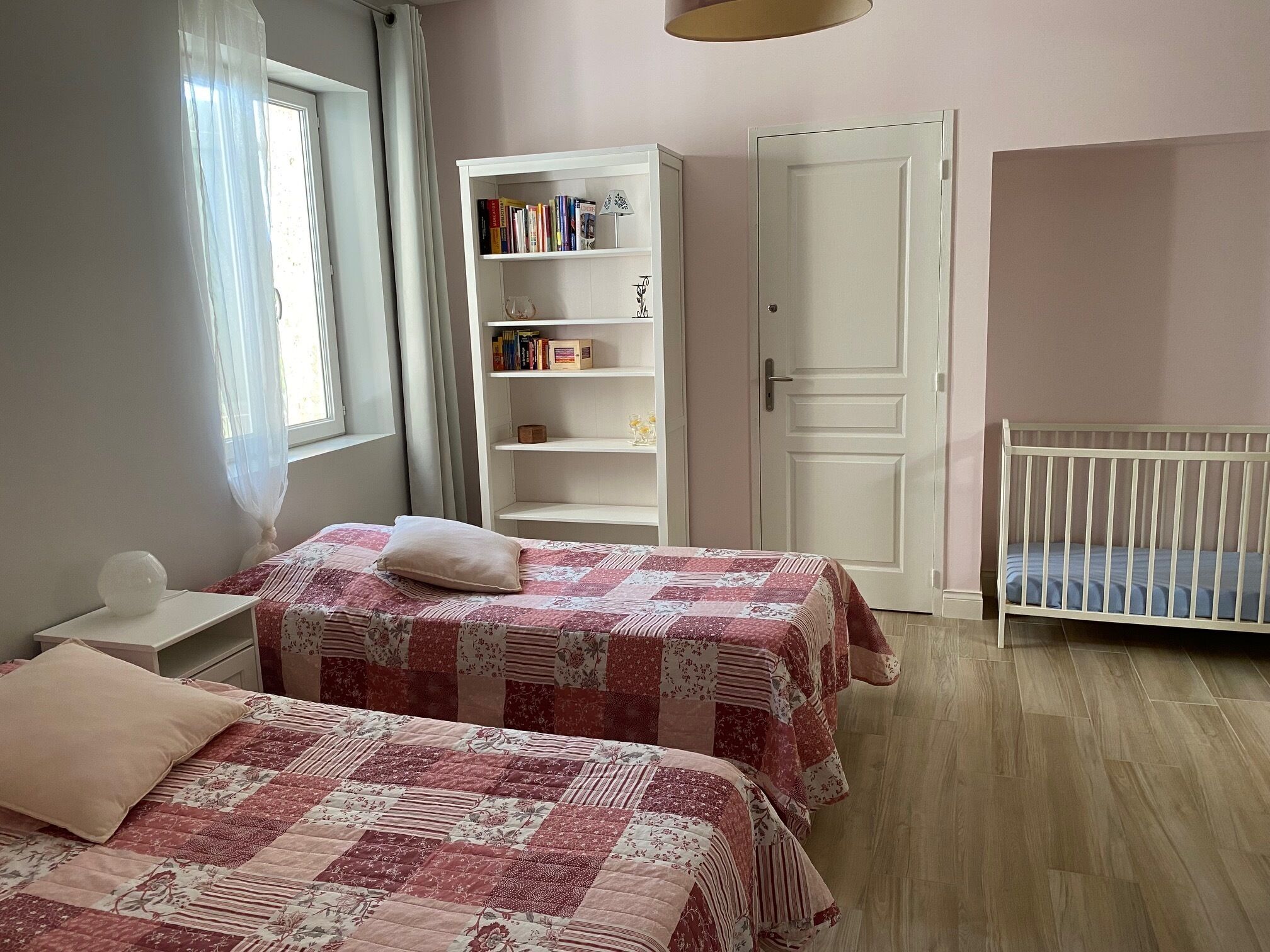 A bedroom with two beds, a bookshelf, a door, and a crib.