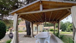 Un área de comedor al aire libre techada, con una pérgola, una mesa preparada para cuatro personas y un sillón colgante.
