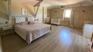Un dormitorio con una cama grande, un radiador blanco, una silla de madera y una pared de piedra.