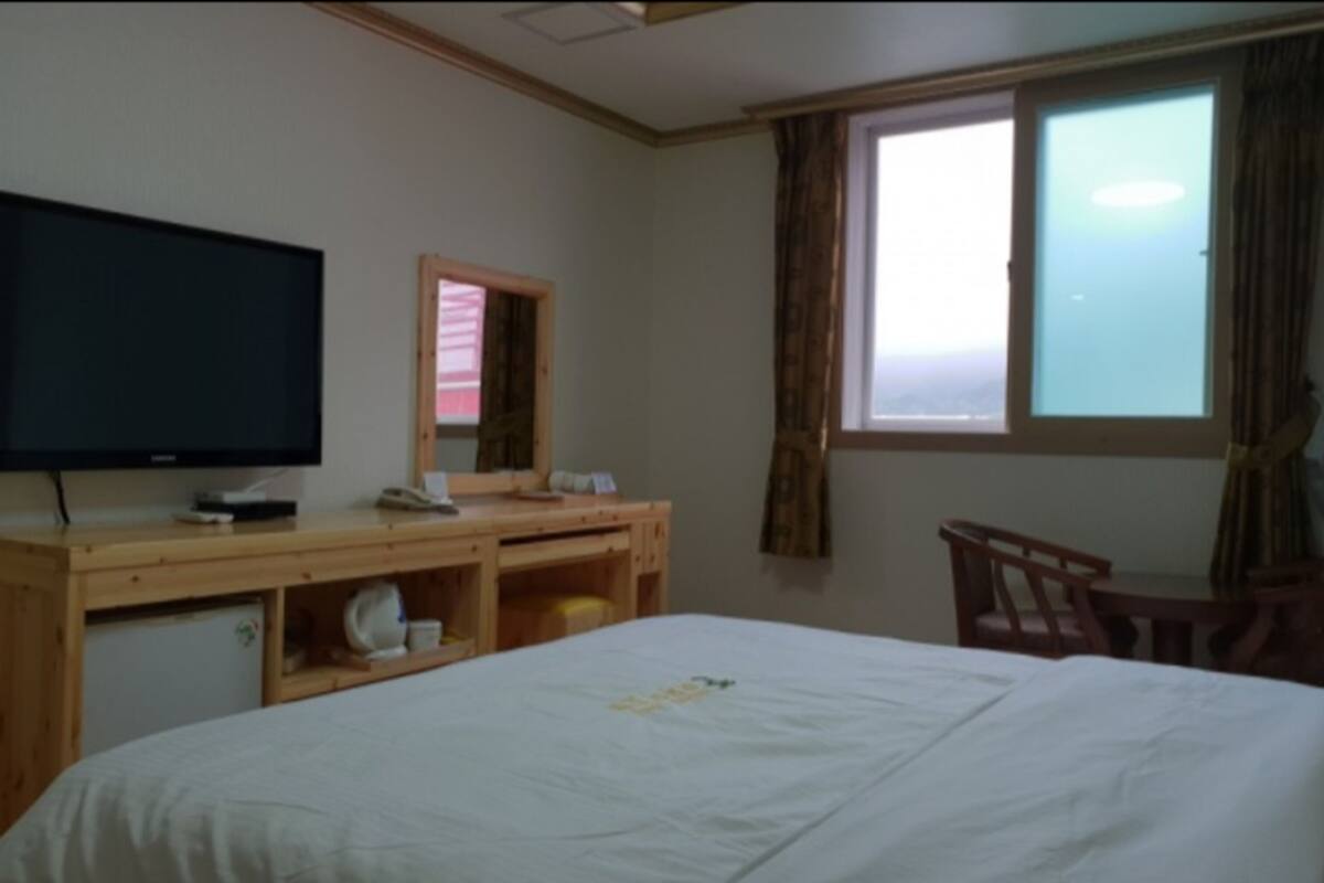 A hotel room with a bed, a desk with a computer, a television, and a window with curtains.