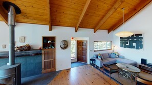 A spacious living area with a wooden ceiling, a built-in fireplace, a sofa, a coffee table, and a large window providing natural light.