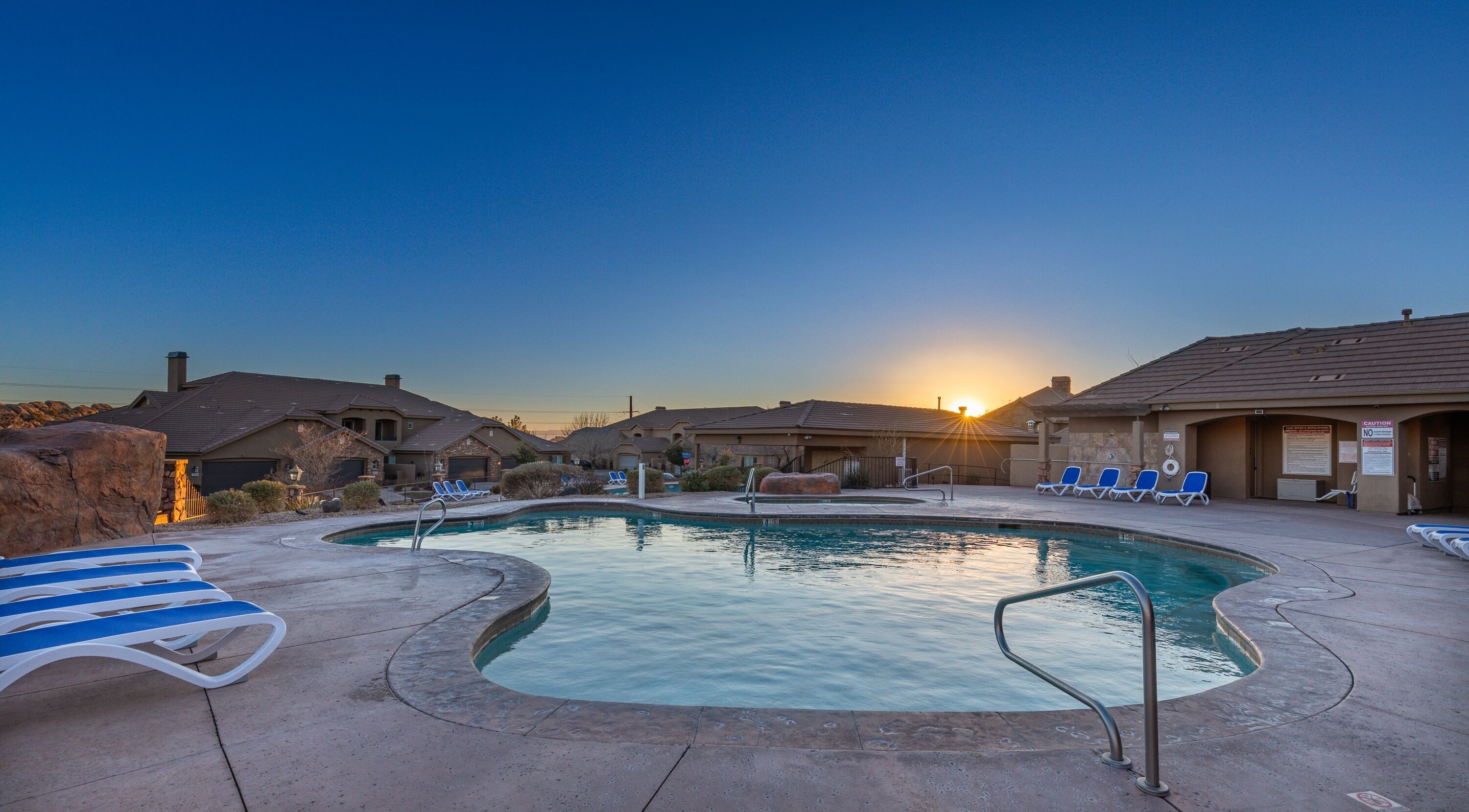 Une piscine avec des chaises longues et un coucher de soleil en arrière-plan.