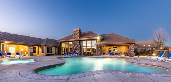 A hotel with a swimming pool, lounge chairs, and a stone facade.