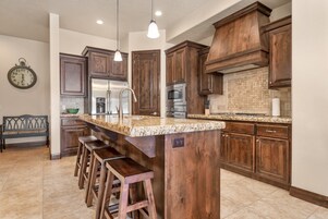 Una cocina con armarios de madera, encimera de granito, refrigerador de acero inoxidable y horno empotrado.