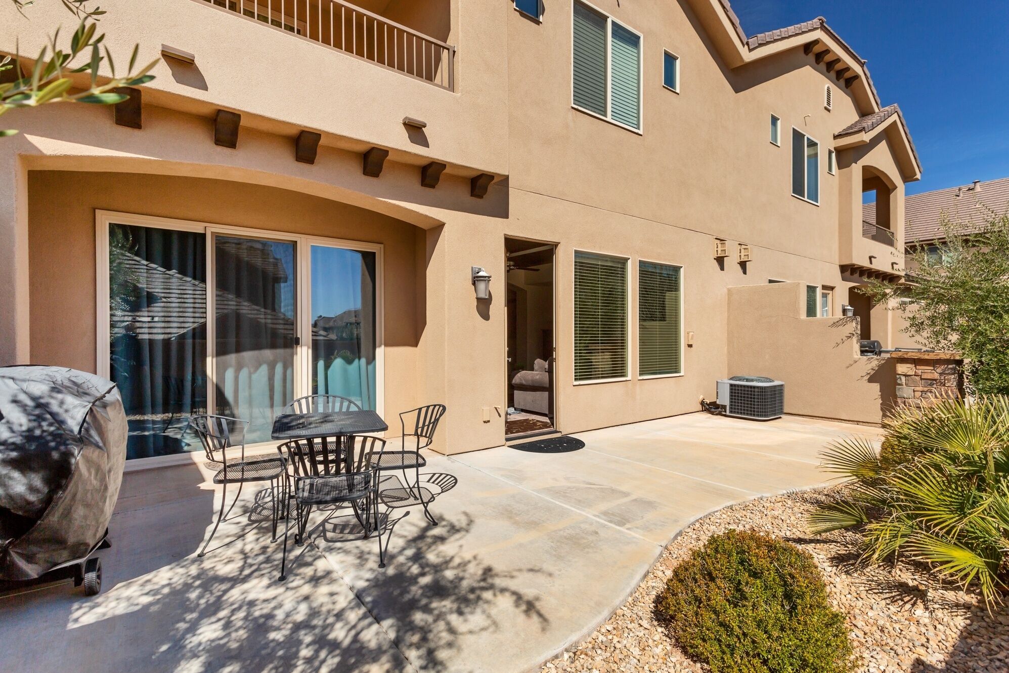 A two-story house with a patio, outdoor furniture, and a covered grill area.