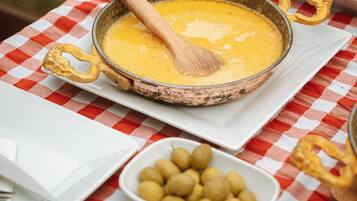 Una mesa con mantel a cuadros, una olla de sopa, un cuenco de aceitunas y un plato de comida.